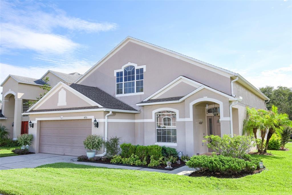 A two-story suburban house with a beige stucco exterior, a two-car garage, and landscaping — 4715 AGUILA PLACE, ORLANDO, FL