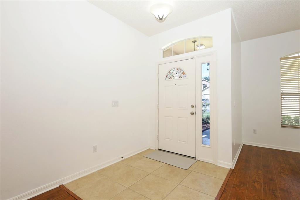 An entryway features a white front door with a sidelight, tile flooring, and white walls — 4715 AGUILA PLACE, ORLANDO, FL