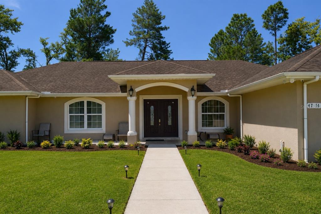 A single-story house with a beige stucco exterior, dark double front doors, and a walkway — 4714 SW 114TH PLACE, OCALA, FL