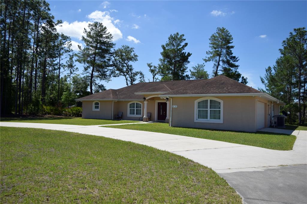 A single-story tan house with a concrete driveway and a large yard surrounded by trees — 4714 SW 114TH PLACE, OCALA, FL