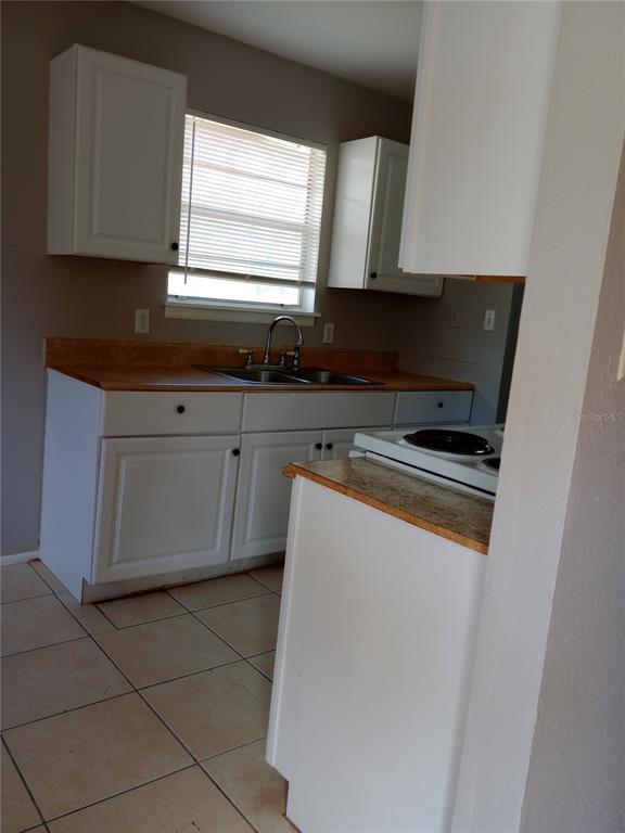 A kitchen features white cabinets, a double-basin sink, tan countertops, and light-colored floor tiles — 2190 KNOX MCRAE DRIVE UNIT F, TITUSVILLE, FL