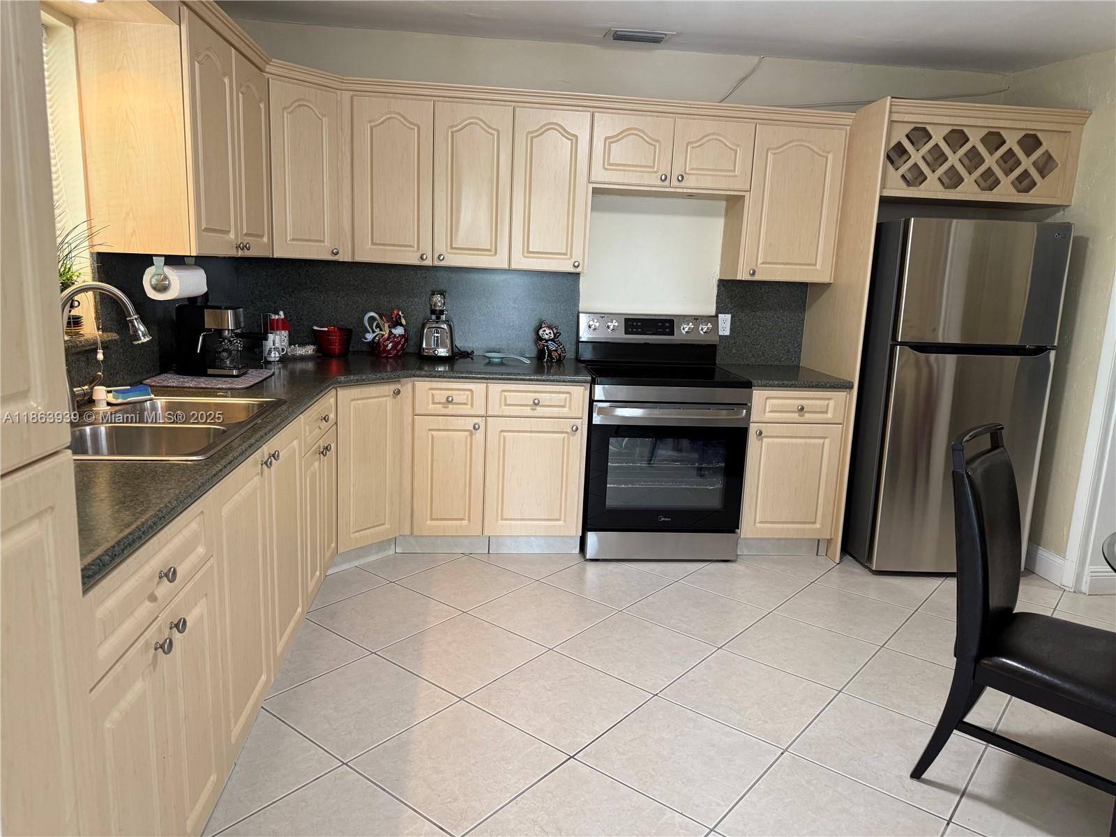 A kitchen features light wood cabinets, stainless steel appliances, dark countertops, and light tile flooring — 6553 SW 148th Pl, Miami FL 33193, MIAMI, FL