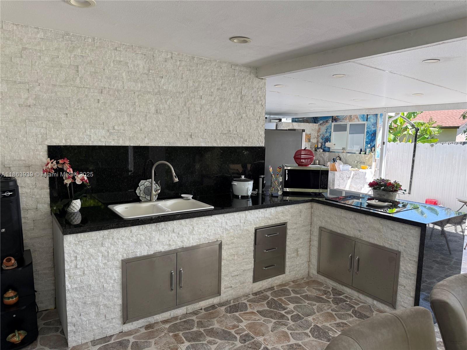 An outdoor kitchen features a black granite countertop, white stone veneer, and stainless steel cabinets — 6553 SW 148th Pl, Miami FL 33193, MIAMI, FL