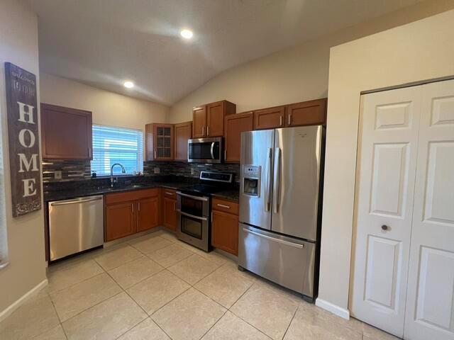 A kitchen features wood cabinets, stainless steel appliances, dark countertops, and light tile flooring — 8583 Vía Serena, Boca Raton FL 33433, BOCA RATON, FL