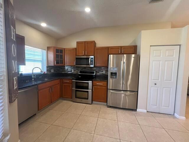 A kitchen features wood cabinets, stainless steel appliances, dark countertops, and tile flooring — 8583 Vía Serena, Boca Raton FL 33433, BOCA RATON, FL
