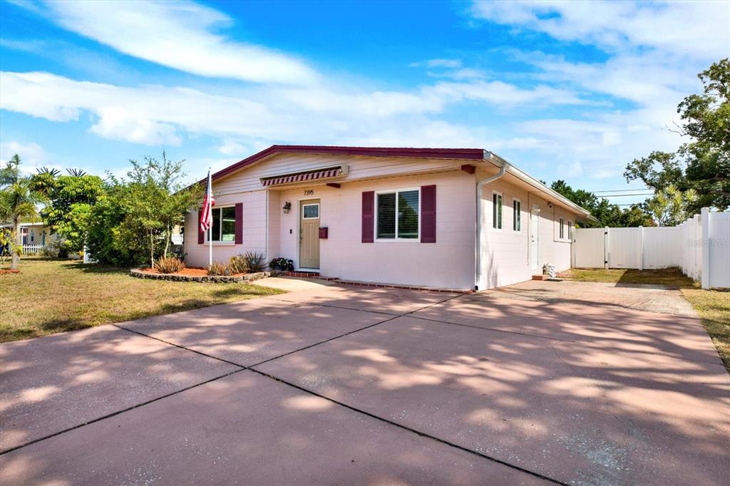A single-story house with light pink siding, a concrete driveway, and a white fence — 7395 18TH STREET N, ST PETERSBURG, FL