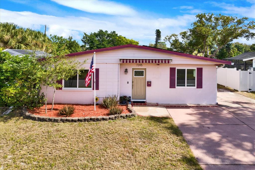 A single-story house with light pink siding, dark purple trim, and a front lawn — 7395 18TH STREET N, ST PETERSBURG, FL