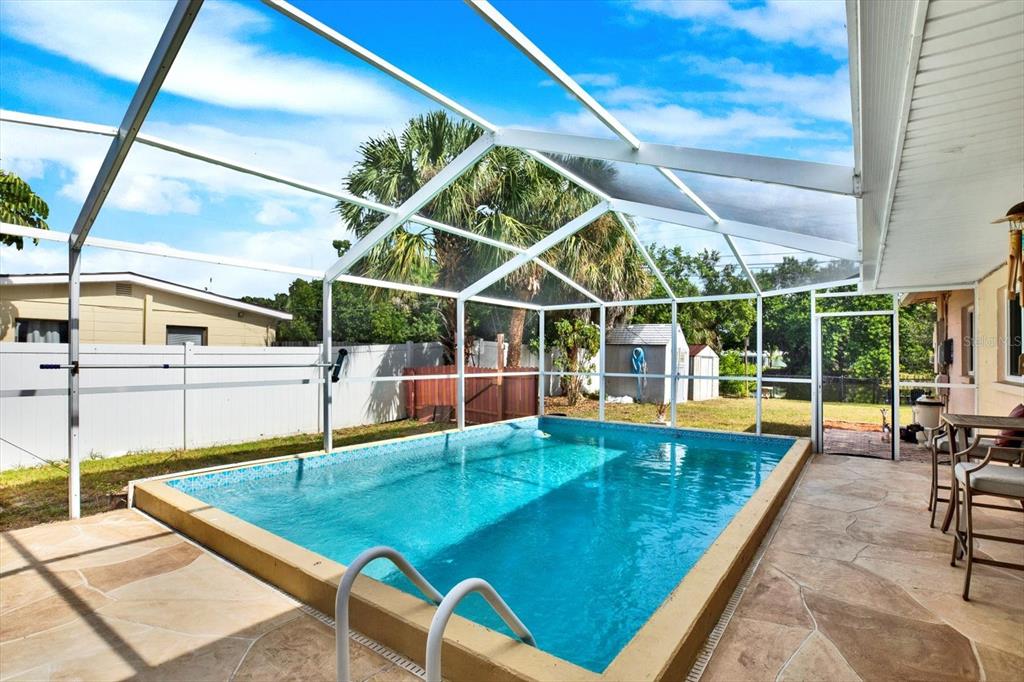 A rectangular swimming pool sits inside a screened-in patio with stone flooring and a fence — 7395 18TH STREET N, ST PETERSBURG, FL