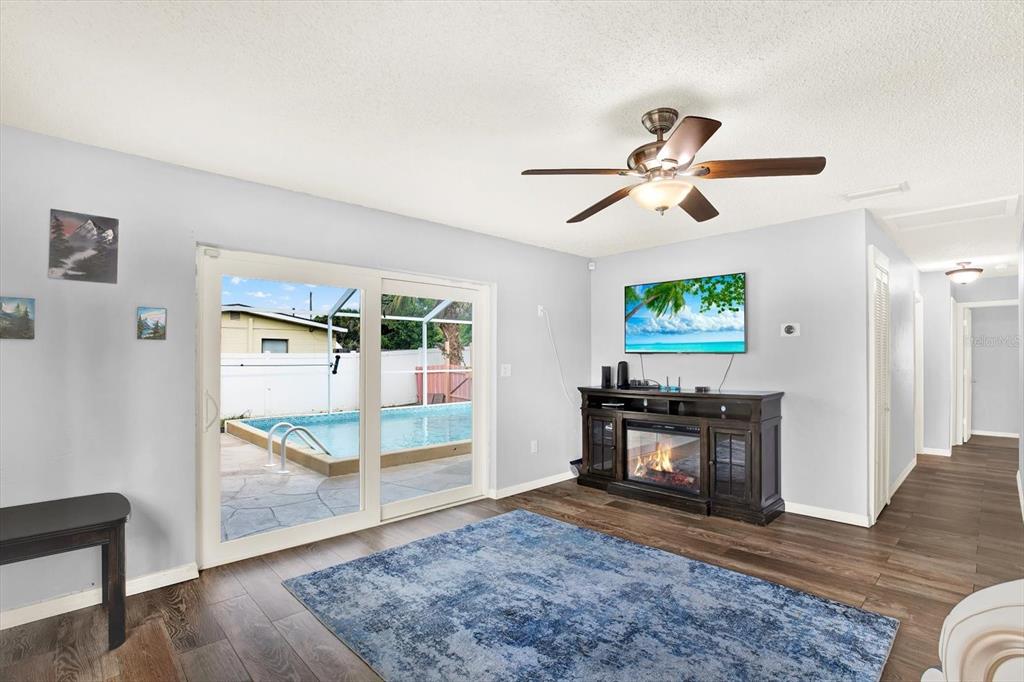 A living room features wood-look flooring, a ceiling fan, a fireplace console, and sliding glass doors — 7395 18TH STREET N, ST PETERSBURG, FL