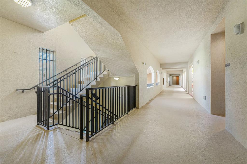 An indoor hallway with a staircase, black metal railings, and textured beige walls — 3311 PURPLE MARTIN DRIVE UNIT 126, PUNTA GORDA, FL