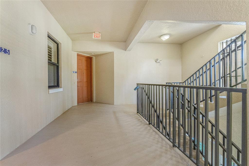 An apartment building hallway features a brown door, a staircase with metal railings, and beige walls — 3311 PURPLE MARTIN DRIVE UNIT 126, PUNTA GORDA, FL