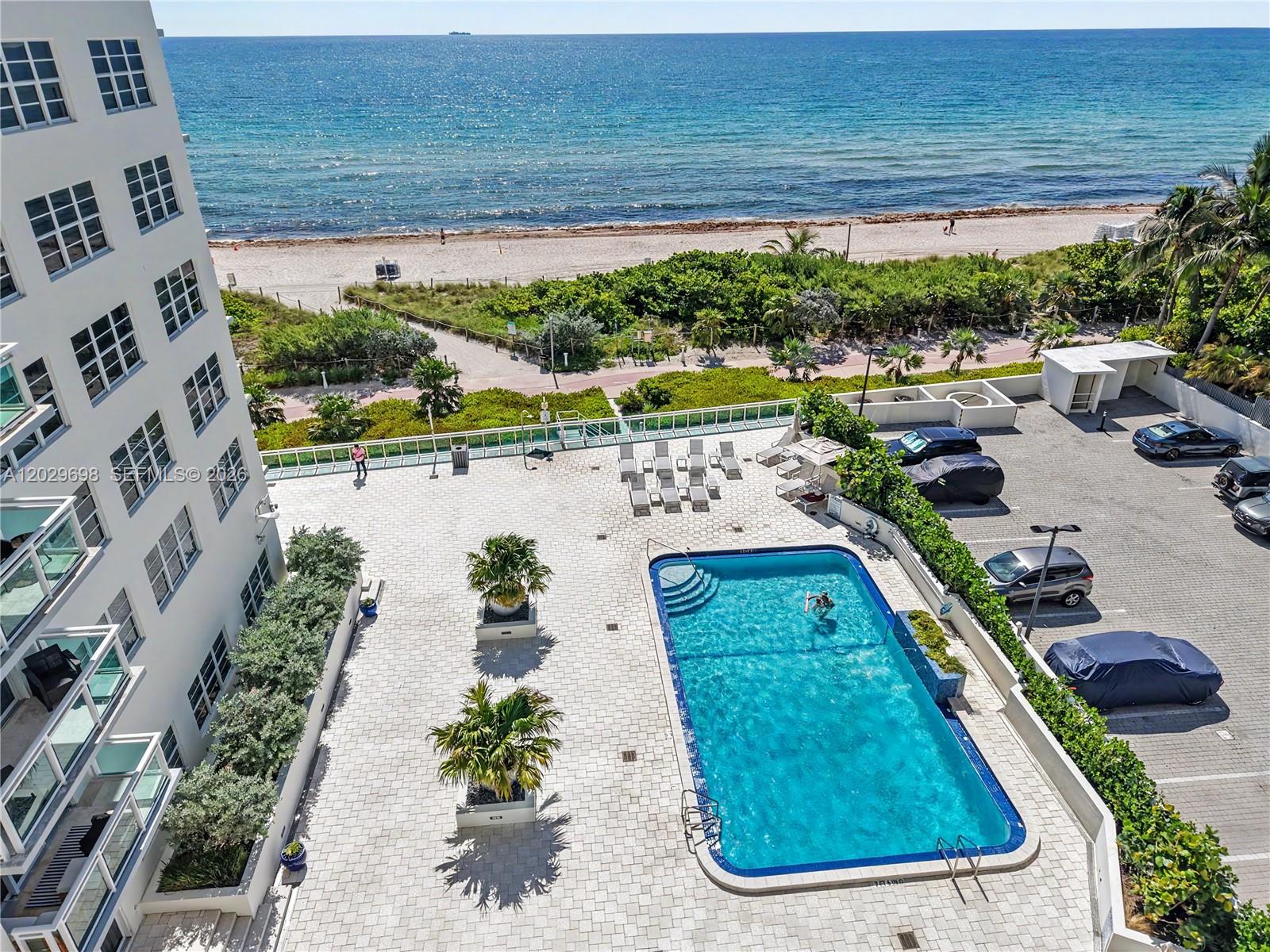 An aerial view shows a swimming pool on a paved deck next to a beach — 6917 Collins Ave # 605, Miami Beach FL 33141, MIAMI BEACH, FL