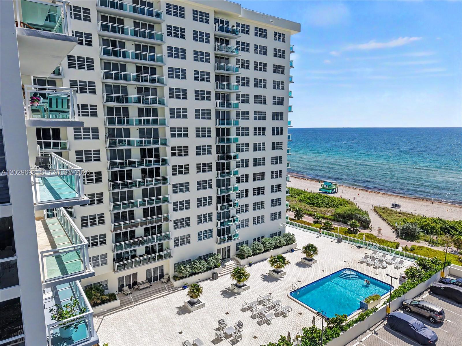 An elevated view shows a high-rise apartment building with balconies overlooking a pool and beach — 6917 Collins Ave # 605, Miami Beach FL 33141, MIAMI BEACH, FL