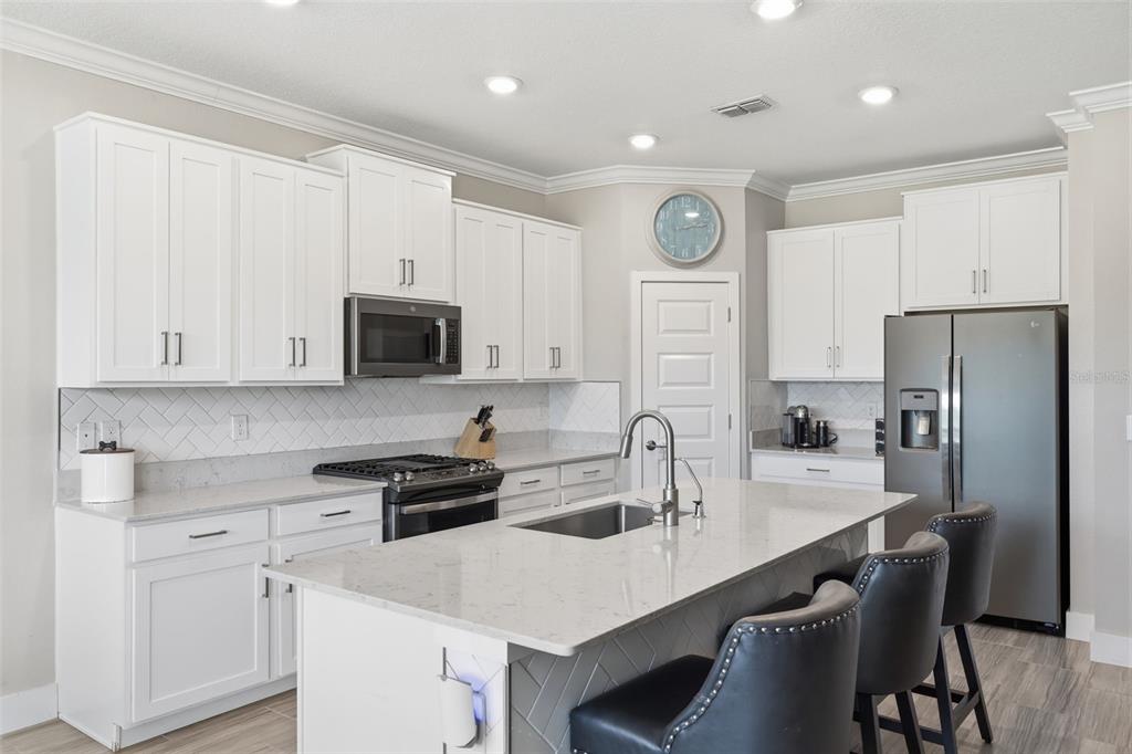 A modern kitchen features white cabinets, quartz countertops, a center island, and stainless steel appliances — 2920 GRIDIRON ISLE, NEW PORT RICHEY, FL