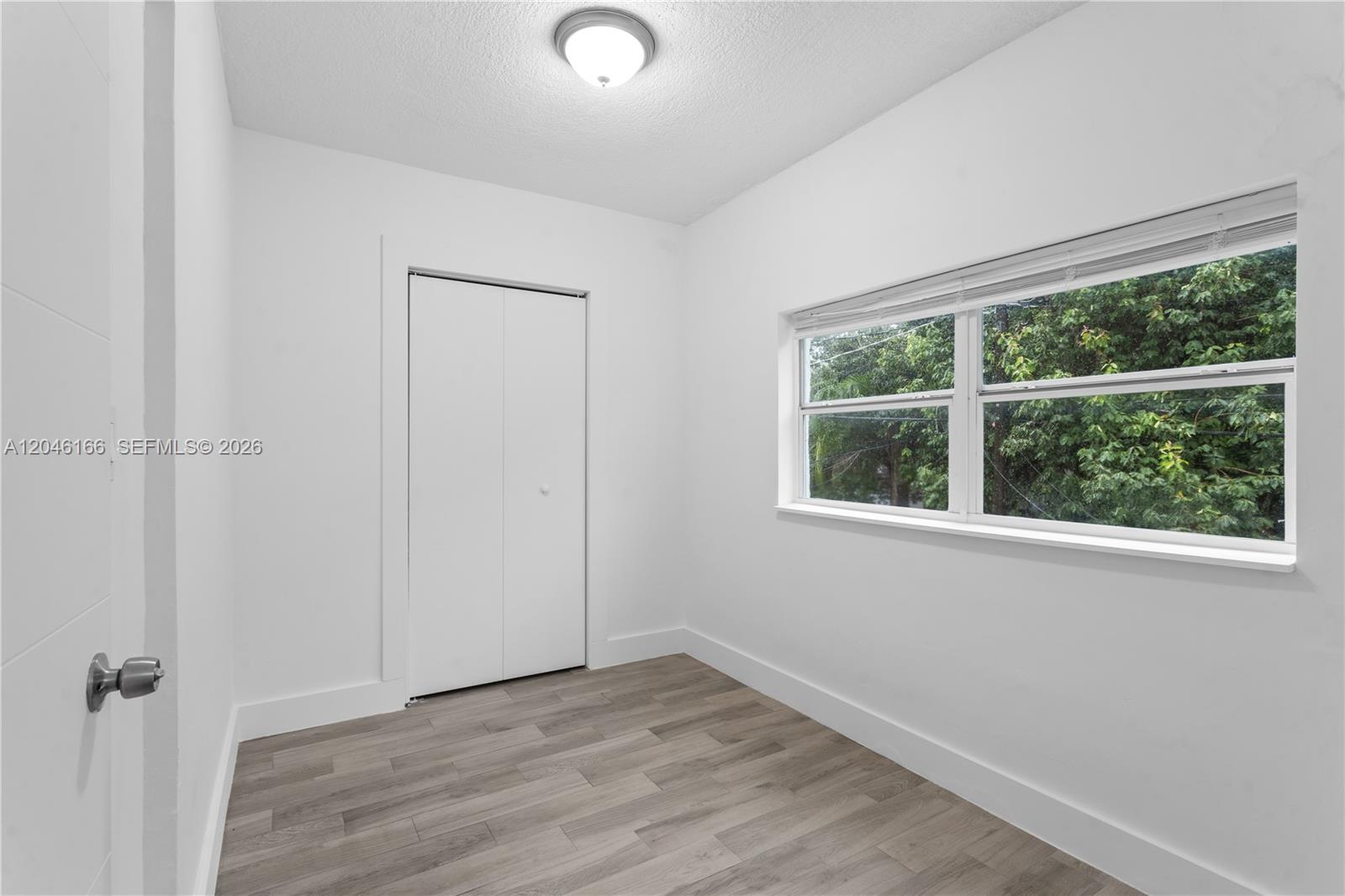 A small bedroom features white walls, light wood-look flooring, a closet, and a large window — 27 NE 60th Ter # 2, Miami FL 33137, MIAMI, FL
