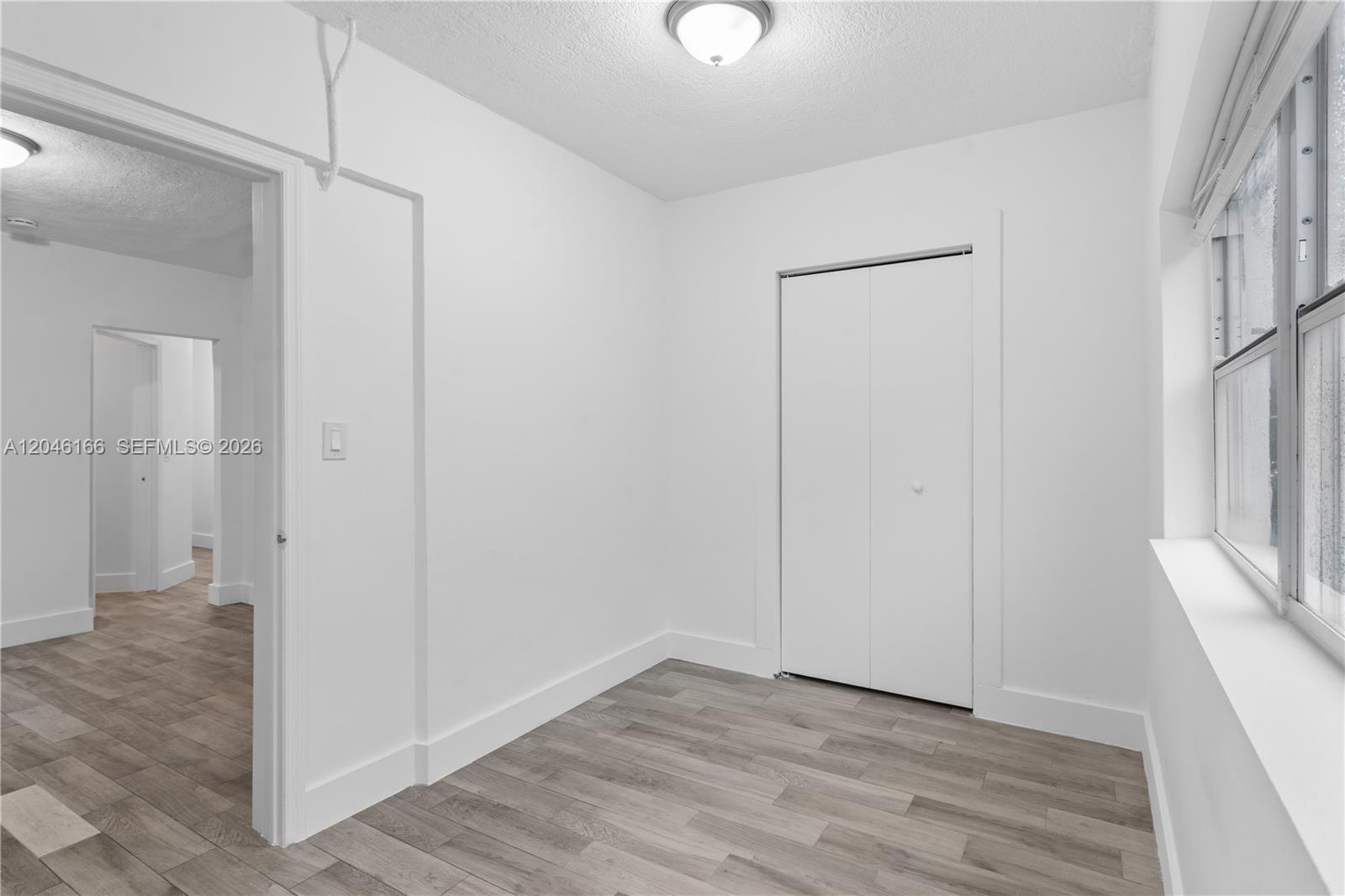 A small, white-walled bedroom features light wood-look flooring, a closet, and a window — 27 NE 60th Ter # 2, Miami FL 33137, MIAMI, FL