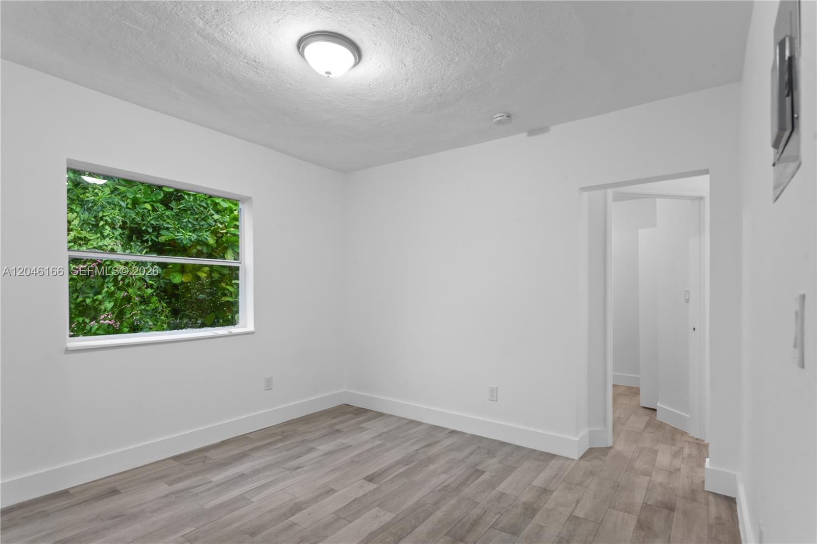 An empty room features white walls, light wood-look flooring, a ceiling light, and a window — 27 NE 60th Ter # 2, Miami FL 33137, MIAMI, FL