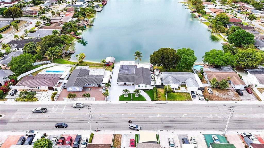 An aerial view shows a row of waterfront houses along a road with parked cars — 6290 W 16th Avenue, Hialeah FL 33012, HIALEAH, FL