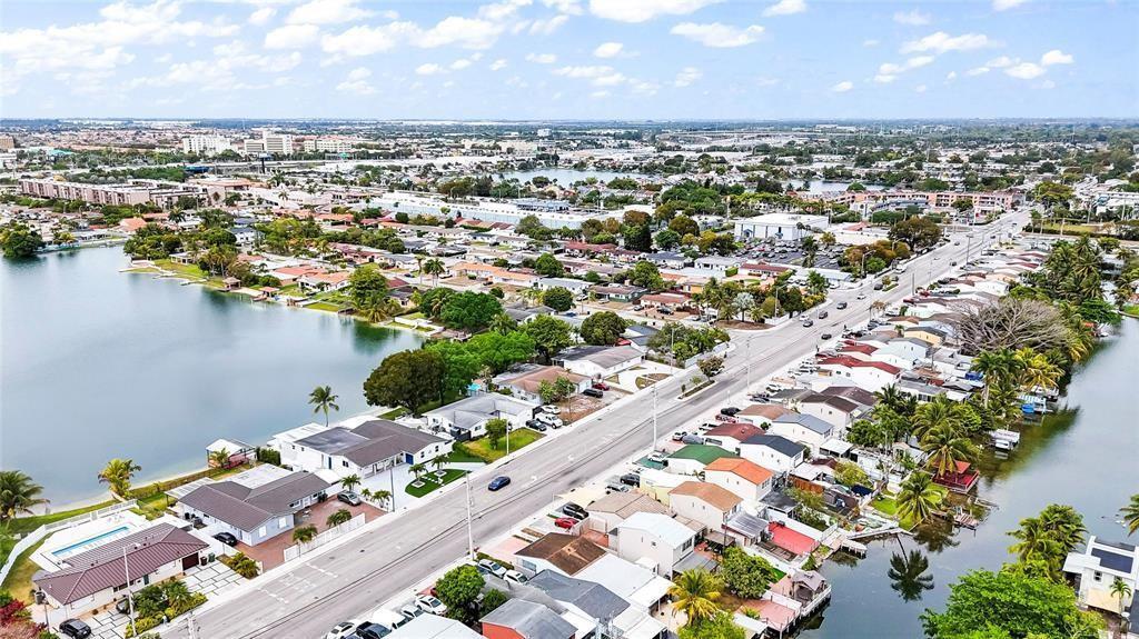 An aerial view shows a suburban neighborhood with houses situated along a lake — 6290 W 16th Avenue, Hialeah FL 33012, HIALEAH, FL