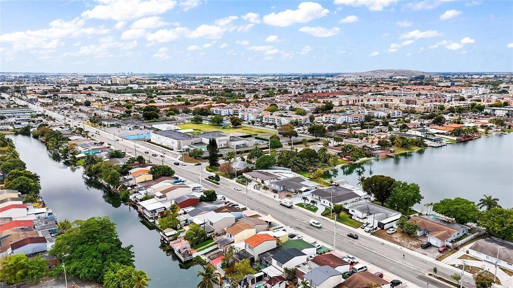 An aerial view shows a suburban neighborhood with houses lining a canal and a road — 6290 W 16th Avenue, Hialeah FL 33012, HIALEAH, FL