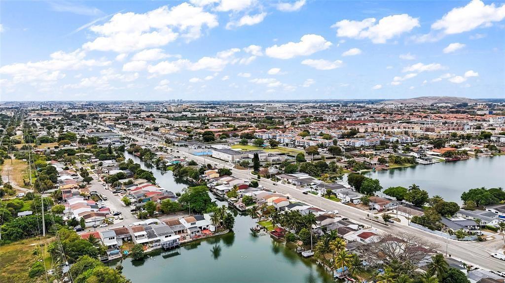 An aerial view shows a suburban neighborhood with houses bordering a lake and roads — 6290 W 16th Avenue, Hialeah FL 33012, HIALEAH, FL