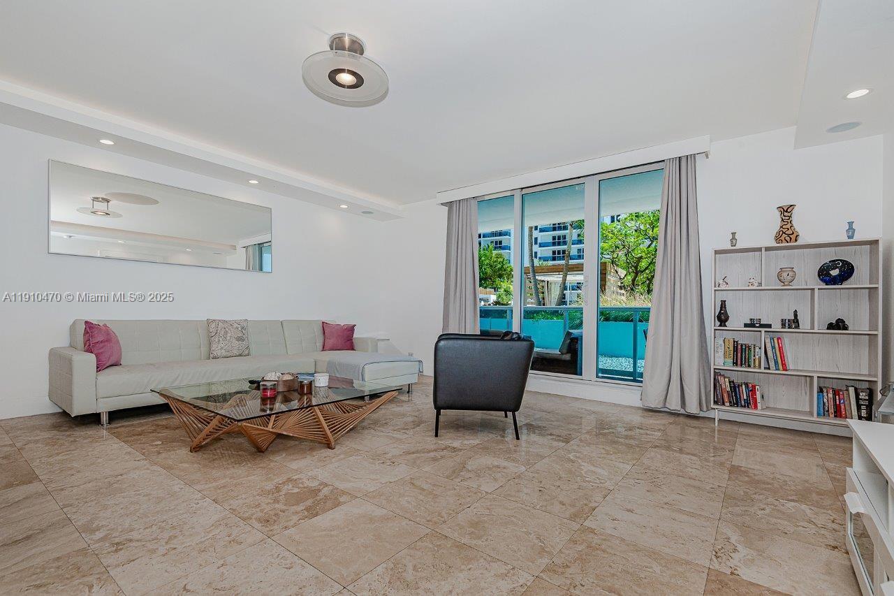 A living room features a beige sectional sofa, glass coffee table, and a bookshelf — 2301 Collins Ave # 310, Miami Beach FL 33139, MIAMI BEACH, FL