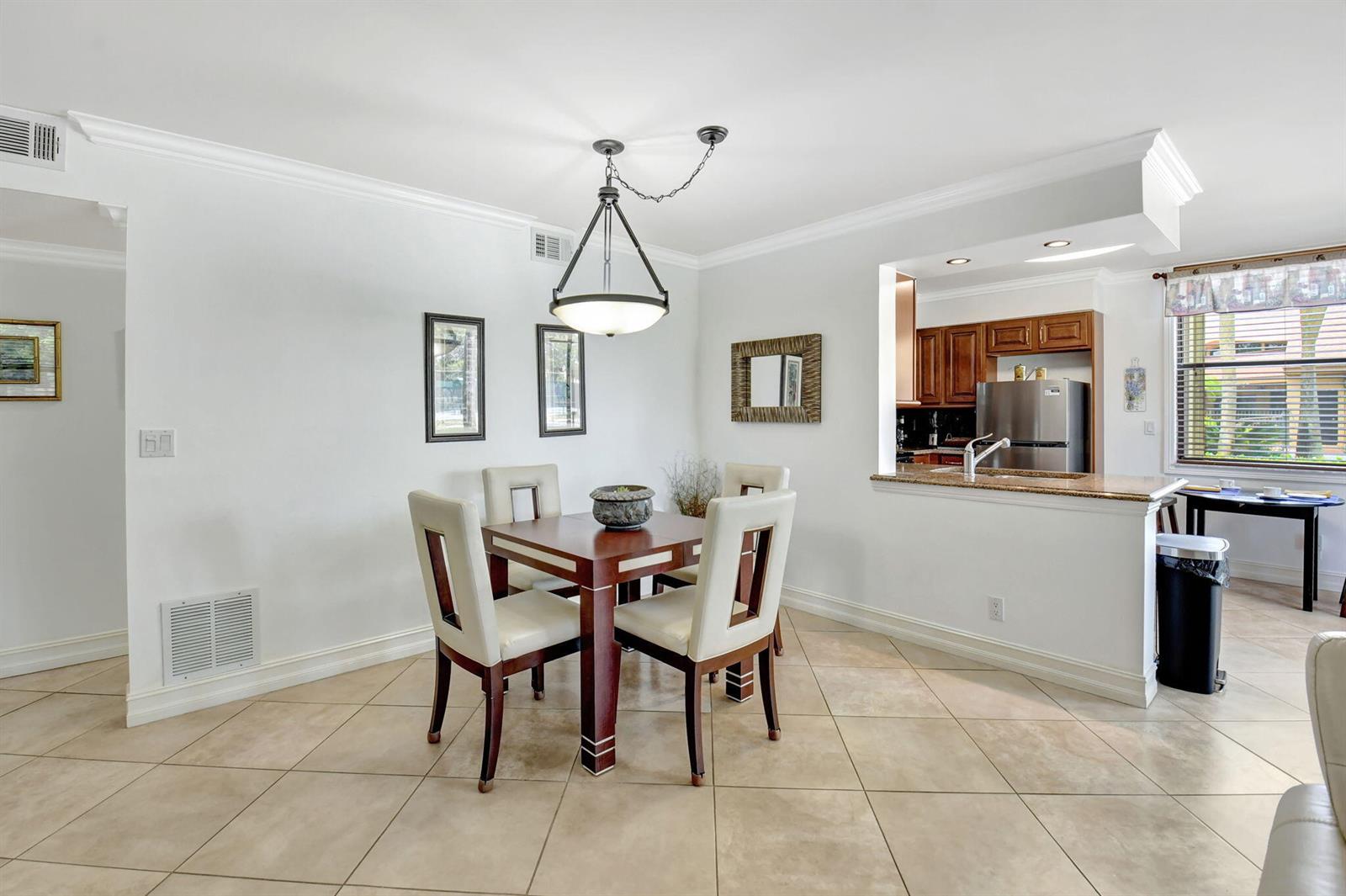 A dining area with a square wooden table, four chairs, and a kitchen pass-through window — 600 Egret Circle # 7105, Delray Beach FL 33444, DELRAY BEACH, FL