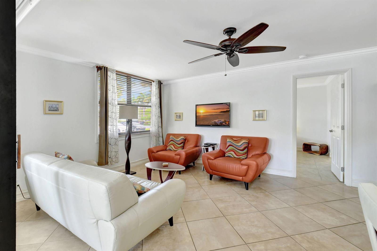 A living room features a white sofa, two orange armchairs, a ceiling fan, and tile flooring — 600 Egret Circle # 7105, Delray Beach FL 33444, DELRAY BEACH, FL