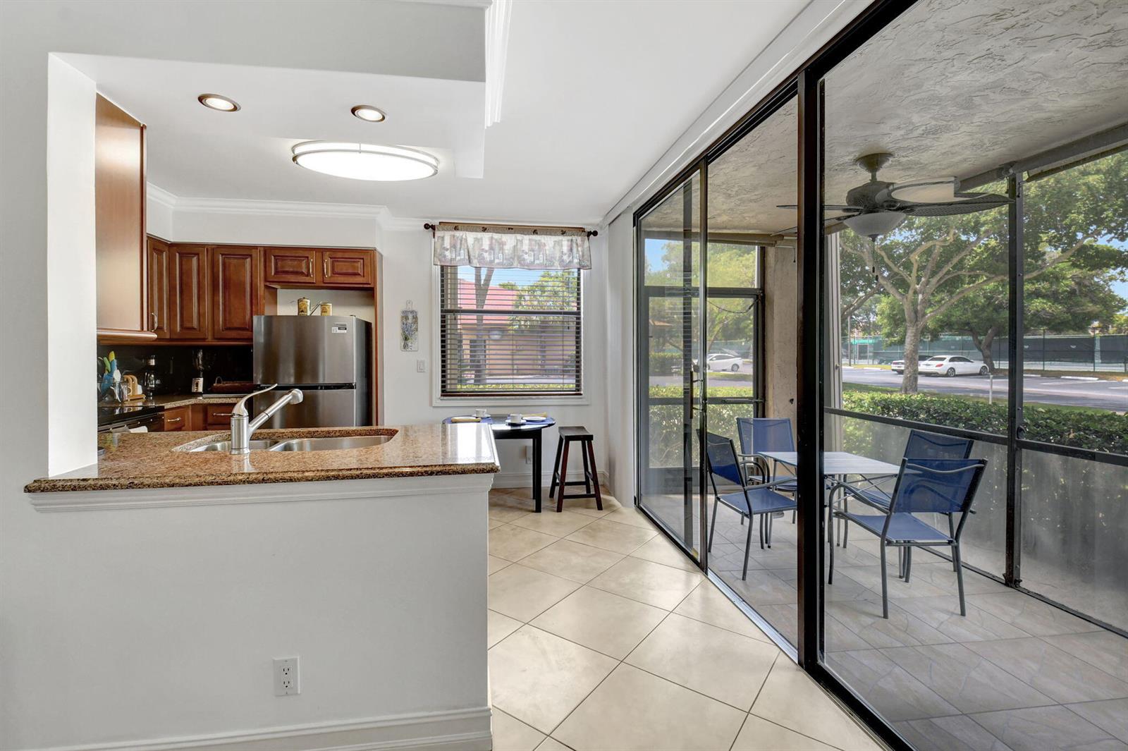 A kitchen with wood cabinets and granite countertops opens to a screened-in patio with seating — 600 Egret Circle # 7105, Delray Beach FL 33444, DELRAY BEACH, FL