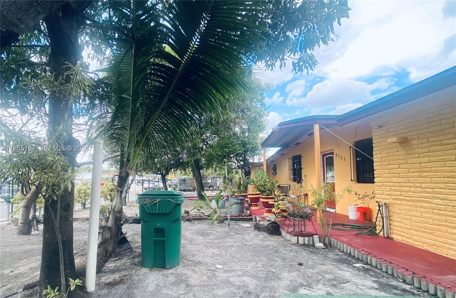 A yellow brick house features a red porch, potted plants, and a green trash bin — 8355 NW 32nd Ave, Miami FL 33147, MIAMI, FL