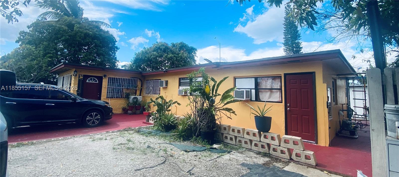 A yellow single-story house features a red door, window air conditioners, and a gravel driveway — 8355 NW 32nd Ave, Miami FL 33147, MIAMI, FL