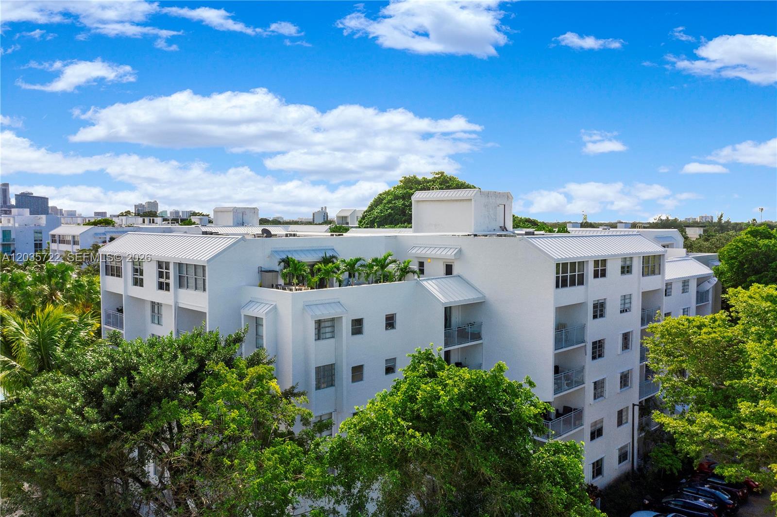 An exterior view of a multi-story white apartment building surrounded by lush green trees — 750 NE 64th St # B314, Miami FL 33138, MIAMI, FL