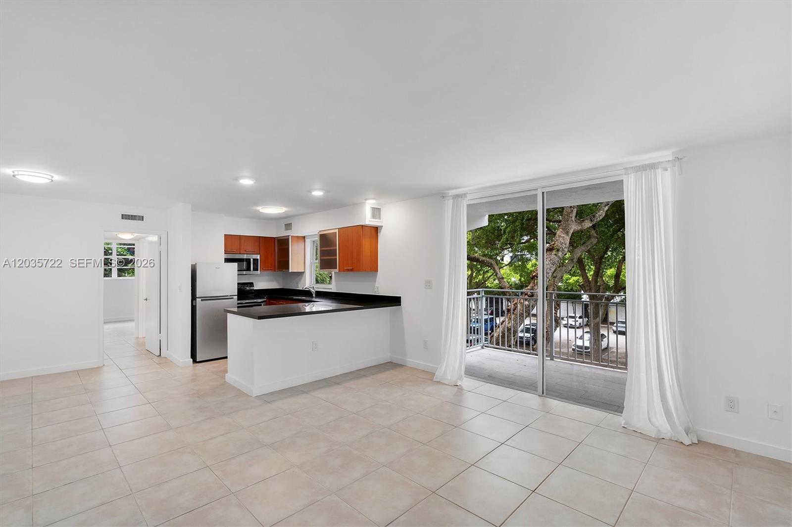 An open-concept kitchen with wood cabinets and a balcony overlooking trees and a parking lot — 750 NE 64th St # B314, Miami FL 33138, MIAMI, FL