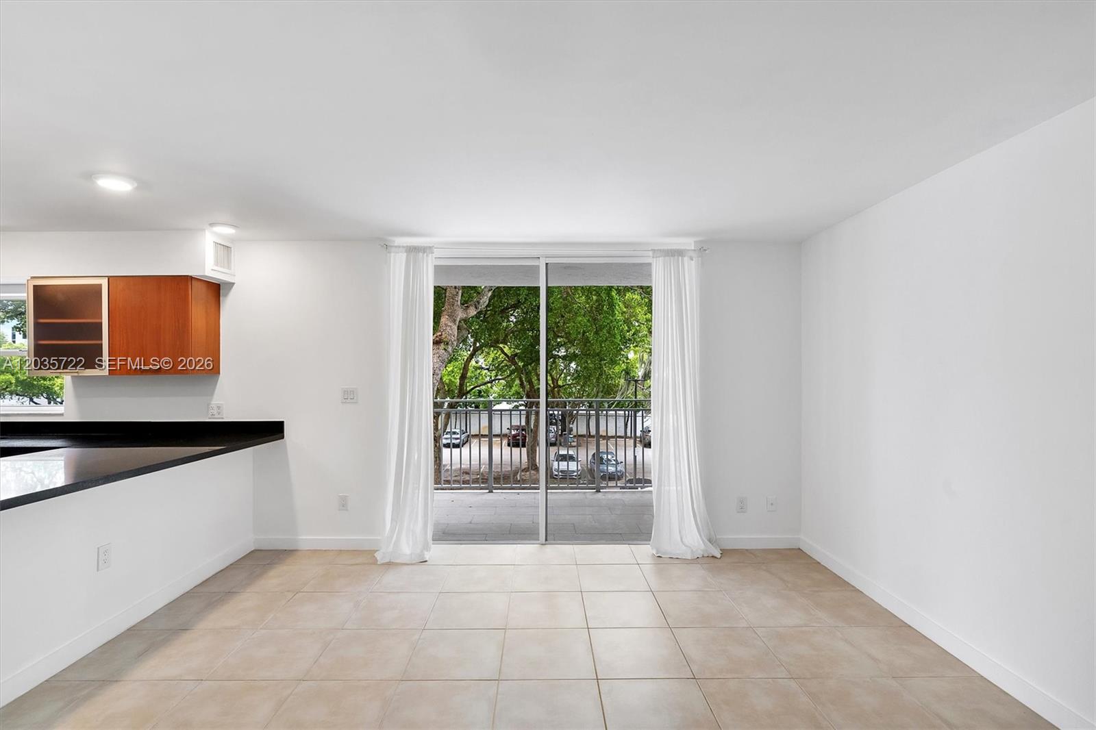 A bright room with tile flooring, a kitchen counter, and sliding doors leading to a balcony — 750 NE 64th St # B314, Miami FL 33138, MIAMI, FL