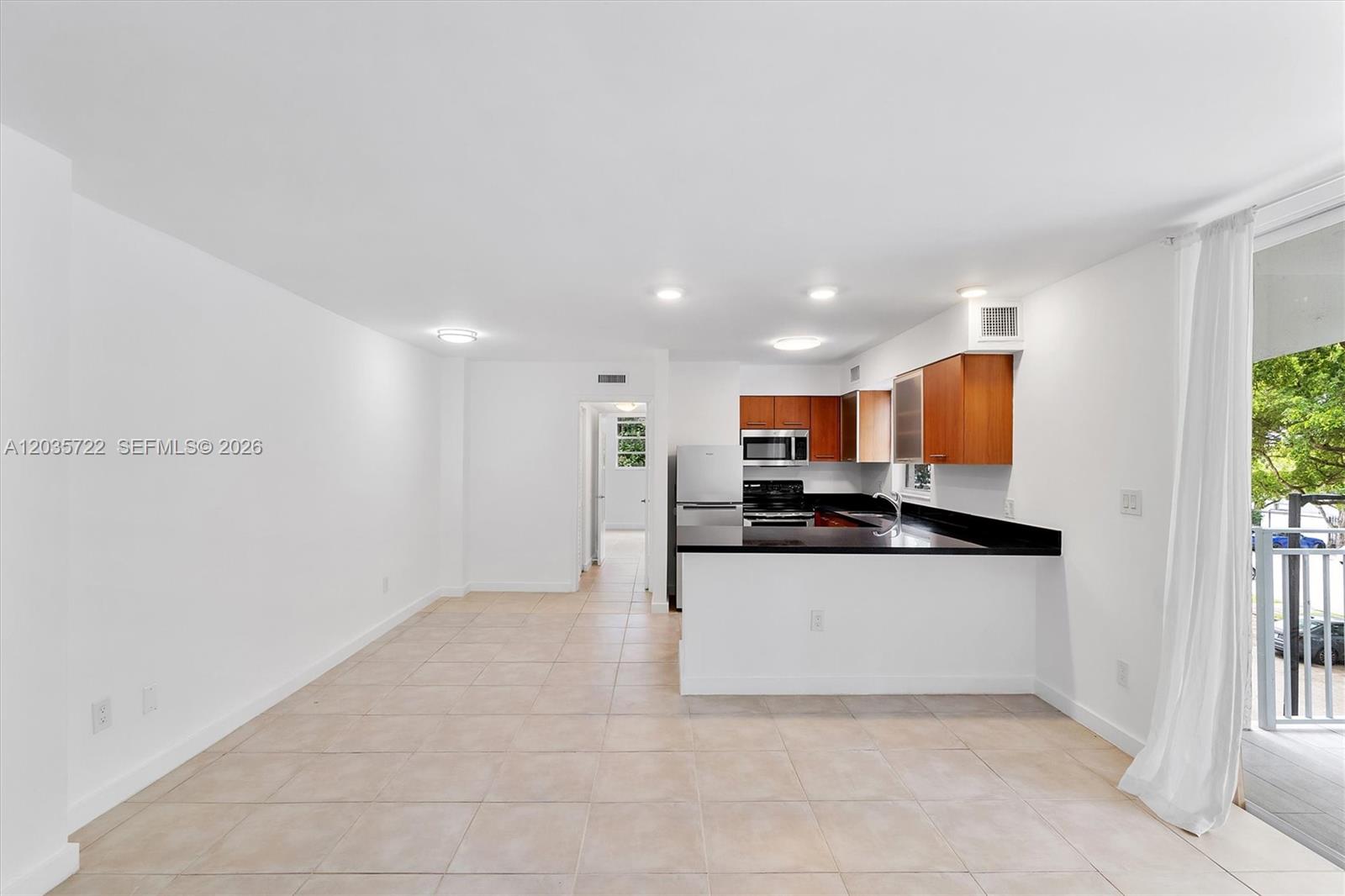 An open-concept kitchen with dark countertops and wood cabinets overlooks a tiled living area — 750 NE 64th St # B314, Miami FL 33138, MIAMI, FL