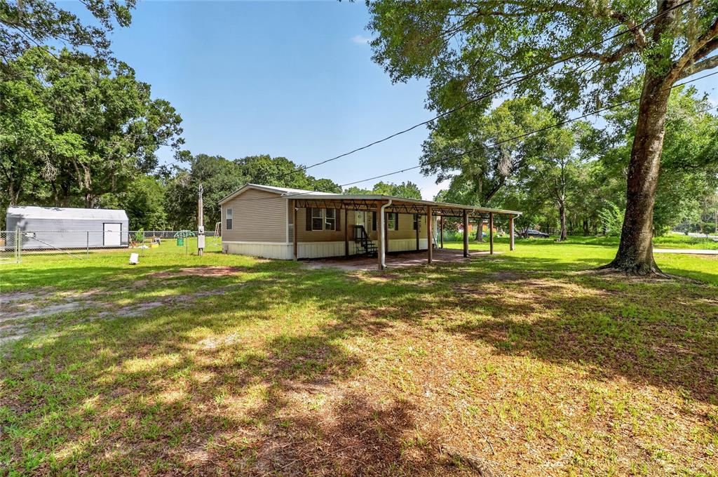 A single-story manufactured home with a covered porch sits on a large, grassy, wooded lot — 1708 ROBIN STREET, AUBURNDALE, FL