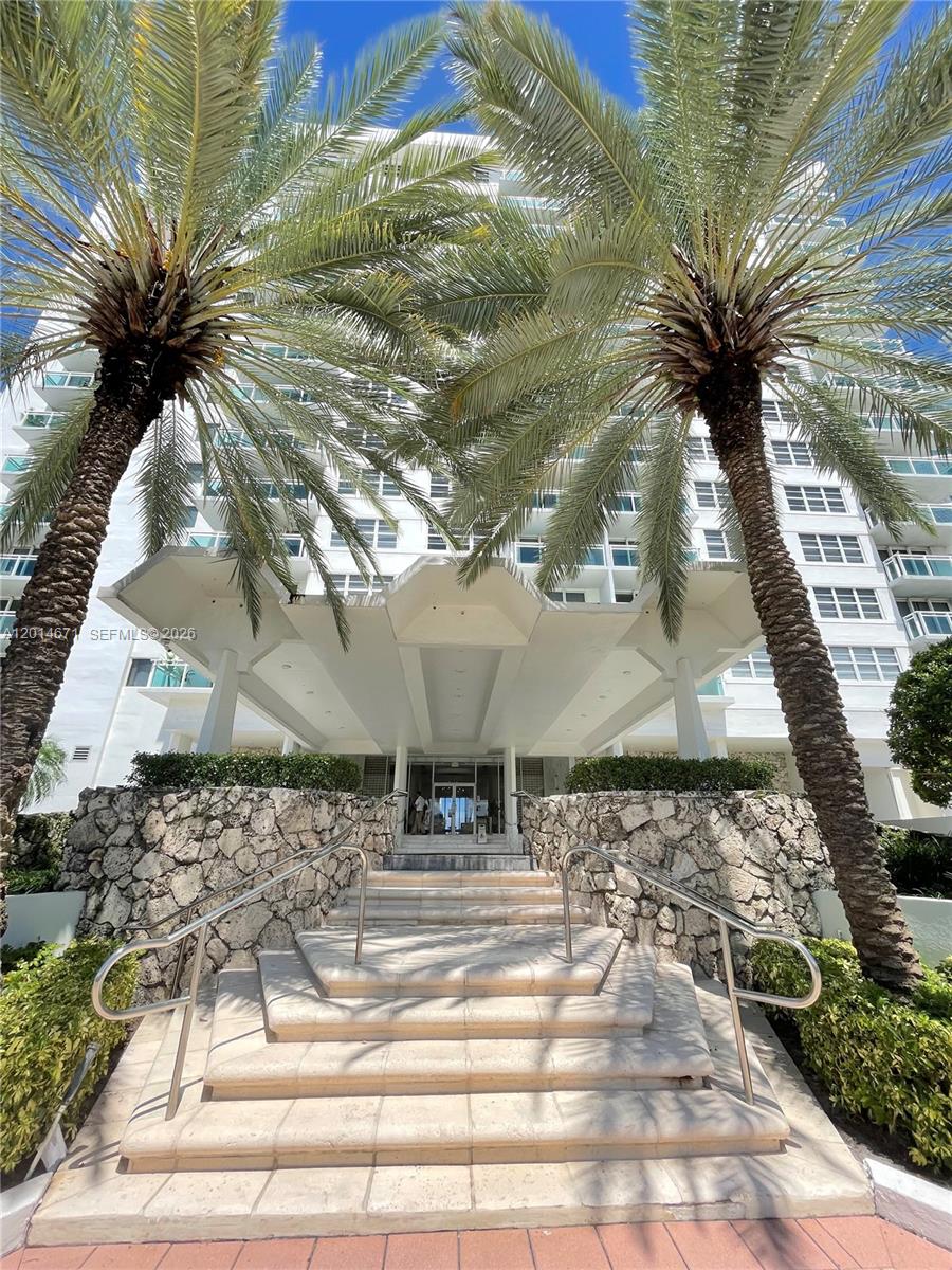 A stone-walled staircase leads to the entrance of a white high-rise building with palm trees — 6917 Collins Ave # 614, Miami Beach FL 33141, MIAMI BEACH, FL