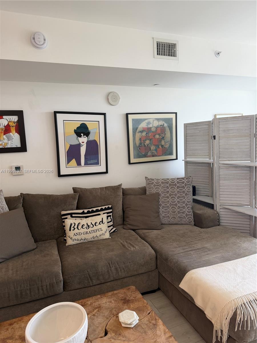 This living room features light wood-look flooring, a wall-mounted television, and an open kitchen — 4250 Biscayne Blvd # 1115, Miami FL 33137, MIAMI, FL