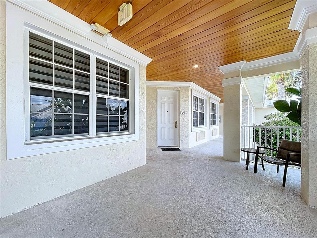 A covered outdoor walkway features a wood-paneled ceiling, white walls, and a white door — 3506 54TH DRIVE W UNIT 207, BRADENTON, FL