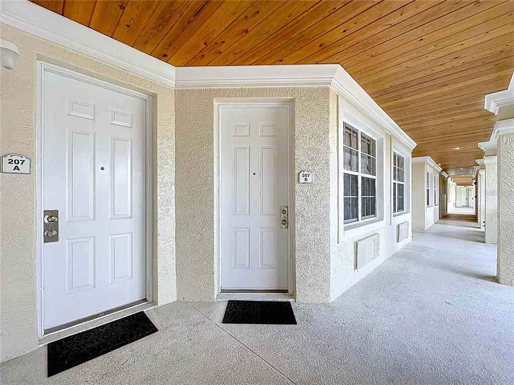Two white entry doors labeled 207A and 207B sit under a wooden ceilinged outdoor walkway — 3506 54TH DRIVE W UNIT 207, BRADENTON, FL