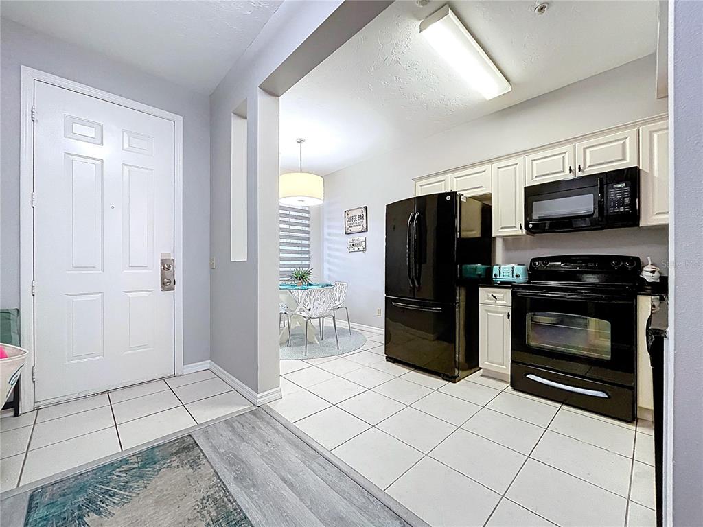 A kitchen with white cabinets and black appliances opens into a dining area — 3506 54TH DRIVE W UNIT 207, BRADENTON, FL