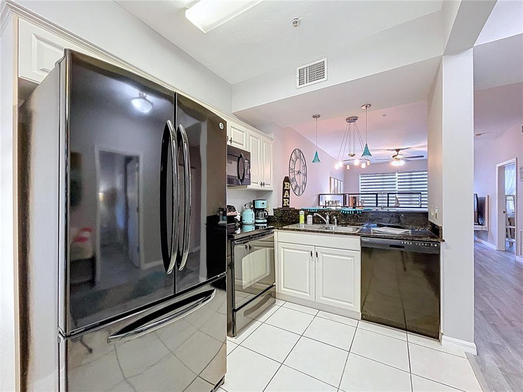 A kitchen features white cabinets, dark countertops, stainless steel appliances, and white tile flooring — 3506 54TH DRIVE W UNIT 207, BRADENTON, FL