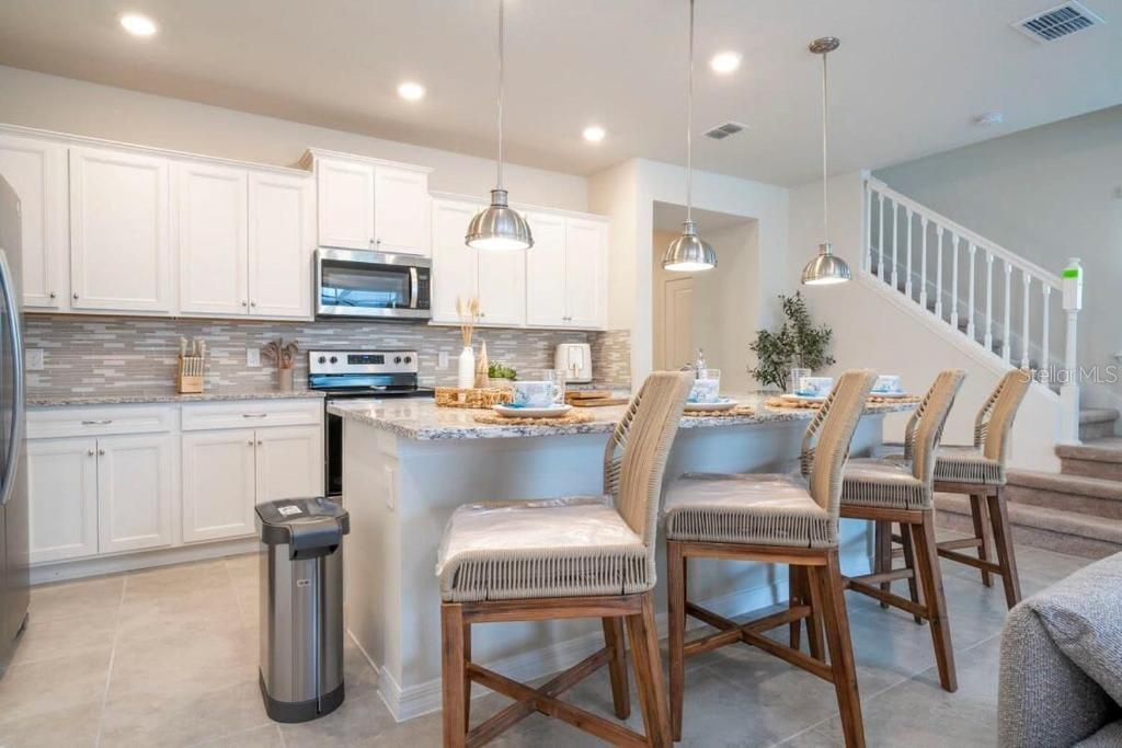 A kitchen with white cabinets, granite countertops, a center island, and three woven bar stools — 4106 LANA AVENUE, DAVENPORT, FL