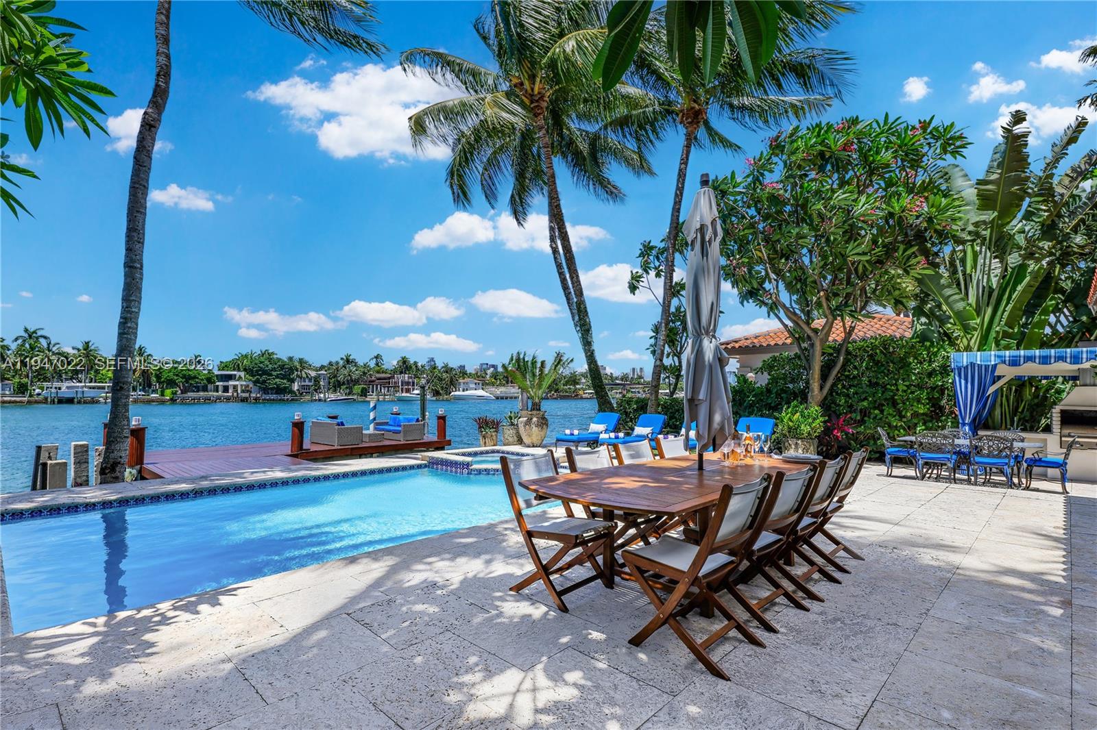A waterfront patio features a swimming pool, dining table, and lounge chairs under palm trees — 56 S Hibiscus Dr, Miami Beach FL 33139, MIAMI BEACH, FL