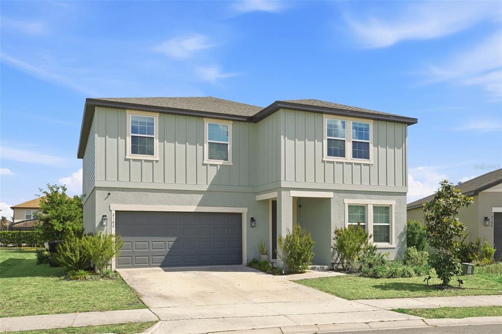 A two-story house with light green vertical siding, a gray garage, and a concrete driveway — 2162 DERWENT DRIVE, DAVENPORT, FL