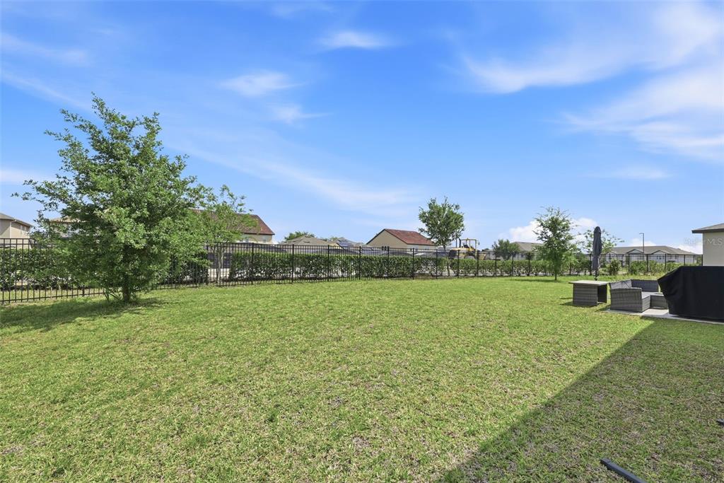 A grassy backyard features a black metal fence, a small tree, and patio furniture — 2162 DERWENT DRIVE, DAVENPORT, FL