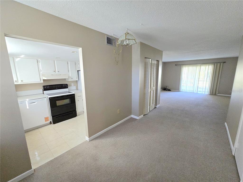 A carpeted living area leads to a kitchen with white cabinets and black appliances — 2727 75TH STREET W UNIT 7A3, BRADENTON, FL