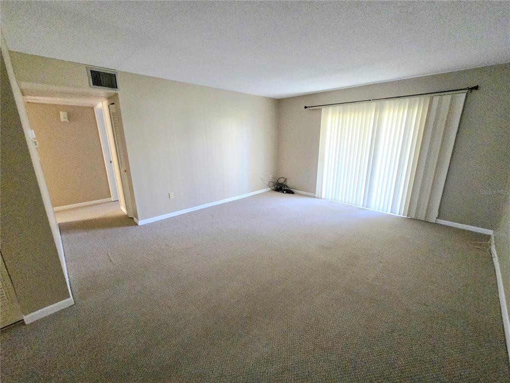 An empty living room features beige carpeting, neutral walls, and a large sliding glass door — 2727 75TH STREET W UNIT 7A3, BRADENTON, FL