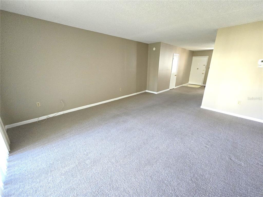 An empty room features beige walls, gray carpeting, and a white door leading to an entryway — 2727 75TH STREET W UNIT 7A3, BRADENTON, FL