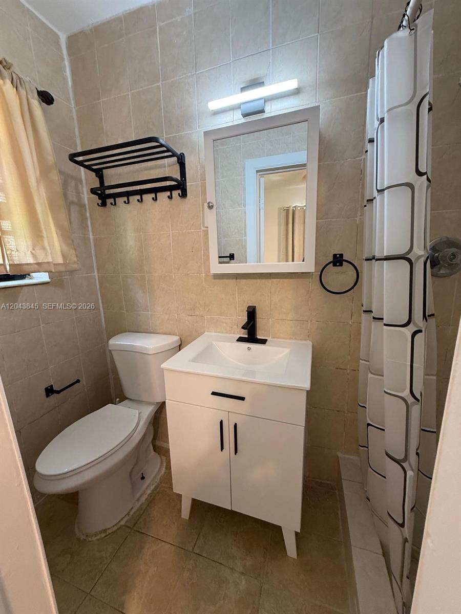 A bathroom features a white vanity, a toilet, a shower curtain, and beige tiled walls — 1301 NE 110th St # 3, Miami FL 33161, MIAMI, FL